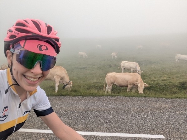 A photo of Julia cycling stage 5 of Le Loop in the Pyrenees with cows and clouds in the background