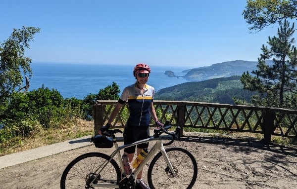 A photo of amateur cyclist Julia with her bike on day 1 of Le Loop with the northern Spanish coast in the background