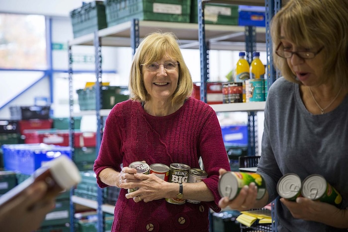 Two warehouse volunteer sort tins of donated food, one of them examining a can of fruit